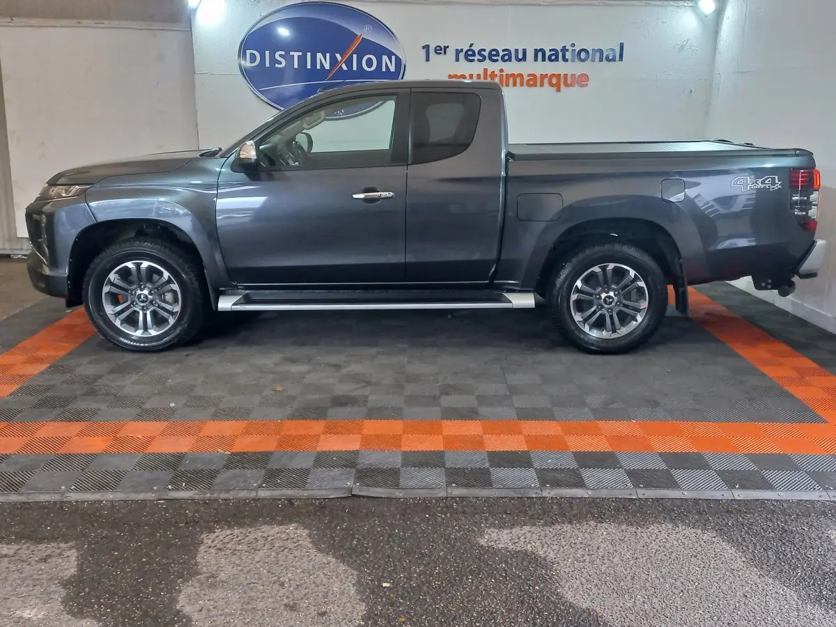 Vue de profil côté gauche d'un pick-up Mitsubishi L200 gris foncé avec jantes alliage et marquage 4x4 à l'arrière.