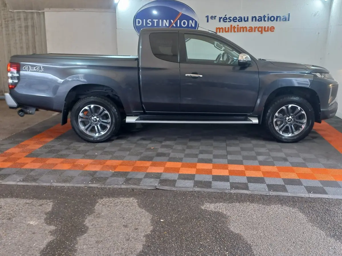 Vue de profil droit d’un pick-up Mitsubishi L200 gris foncé avec jantes alliage et marchepieds latéraux visibles.