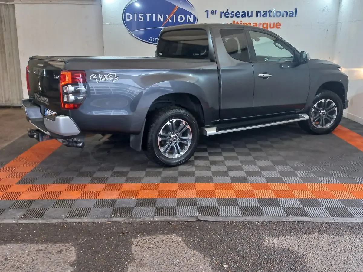 Vue latérale droite d’un pick-up Mitsubishi L200 gris foncé avec benne, jantes alliage et logo 4x4 visible à l’arrière.