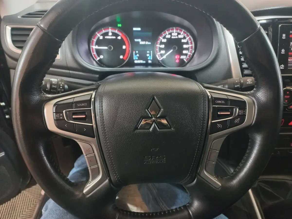 Vue rapprochée du volant cuir noir multifonctions du Mitsubishi L200 2020 avec tableau de bord et compteurs éclairés.