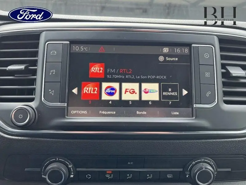 Tableau de bord avec écran tactile multimédia allumé, vue centrale rapprochée, sans visibilité du véhicule blanc.