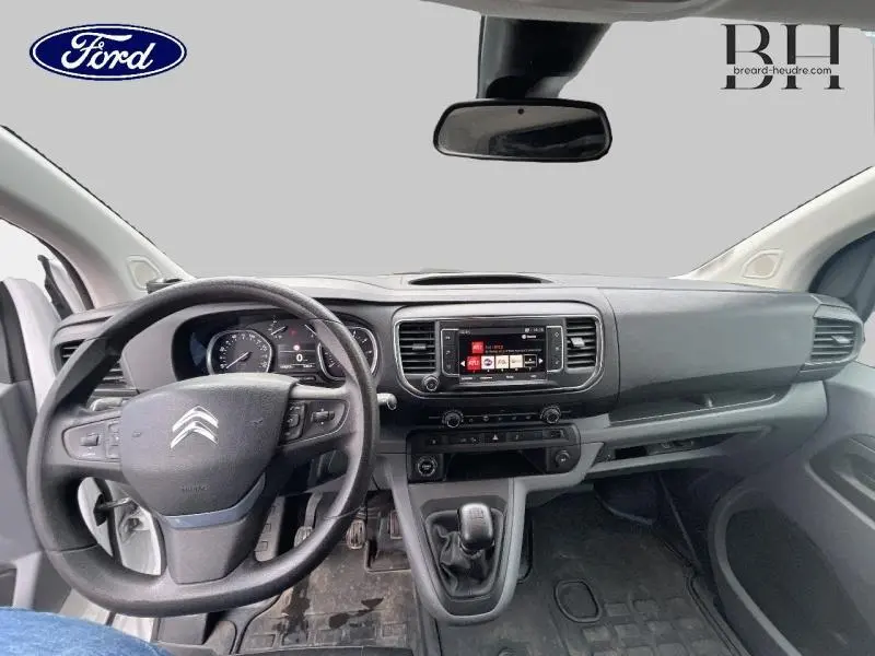 Vue intérieure avant du Citroën Jumpy blanc Banquise de 2016, avec tableau de bord et volant multifonctions visibles.