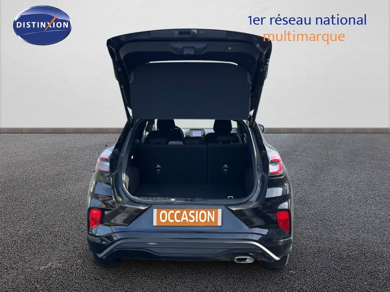 Vue arrière d'un Ford Puma noir Agate Metal 2023 avec hayon ouvert et coffre visible, en extérieur sur sol gris.