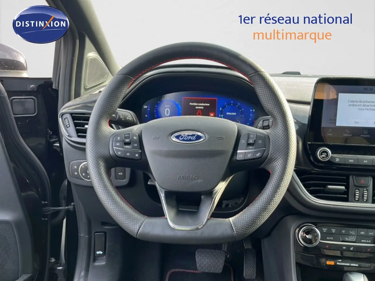Vue intérieure centrée sur le volant perforé noir avec coutures rouges du Ford Puma 2023, tableau de bord et écran tactile visibles.
