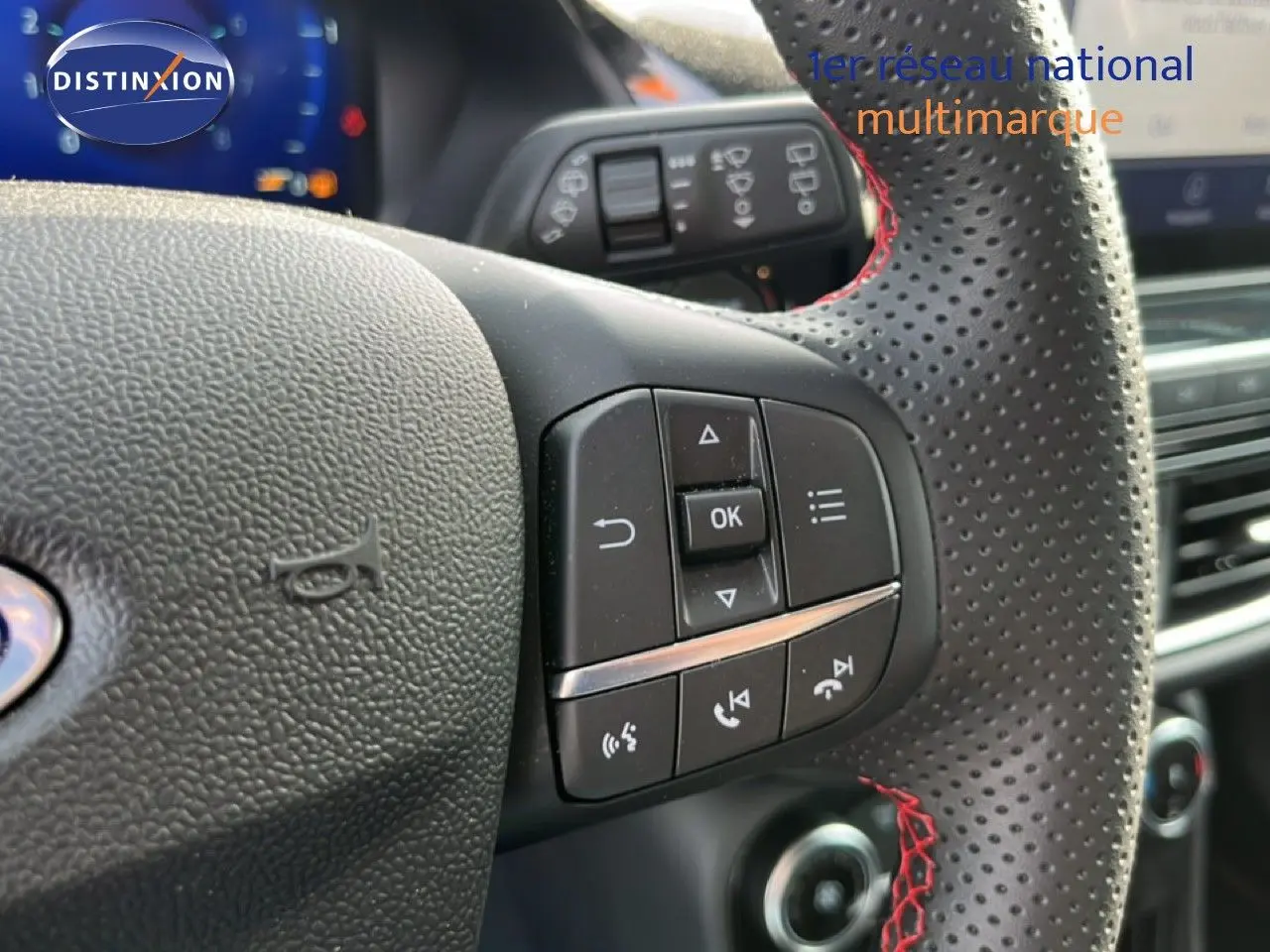 Gros plan sur le volant perforé avec surpiqûres rouges du Ford Puma noir Agate 2023, montrant les commandes multifonctions.