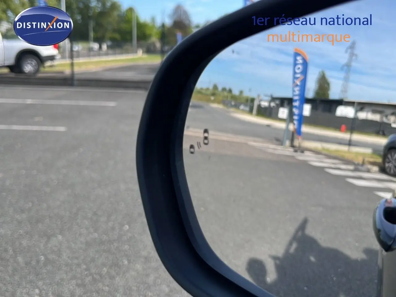 Rétroviseur côté droit d'un Ford Puma noir agate métal 2023, avec reflet d'une route et d'un drapeau Distinxion.