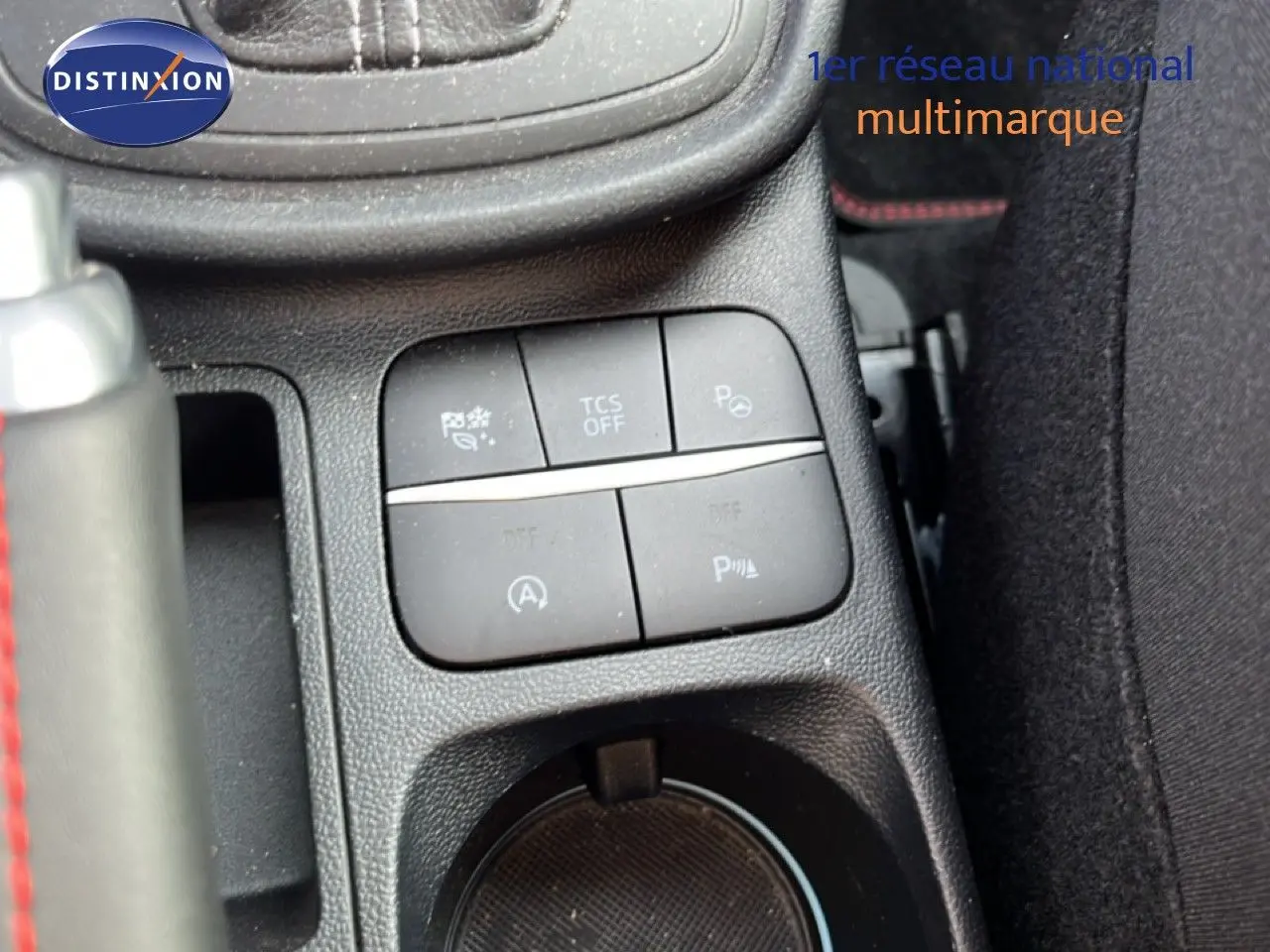 Gros plan sur les commandes centrales et porte-gobelet d’un Ford Puma noir agate métal, intérieur tissu noir avec surpiqûres rouges.