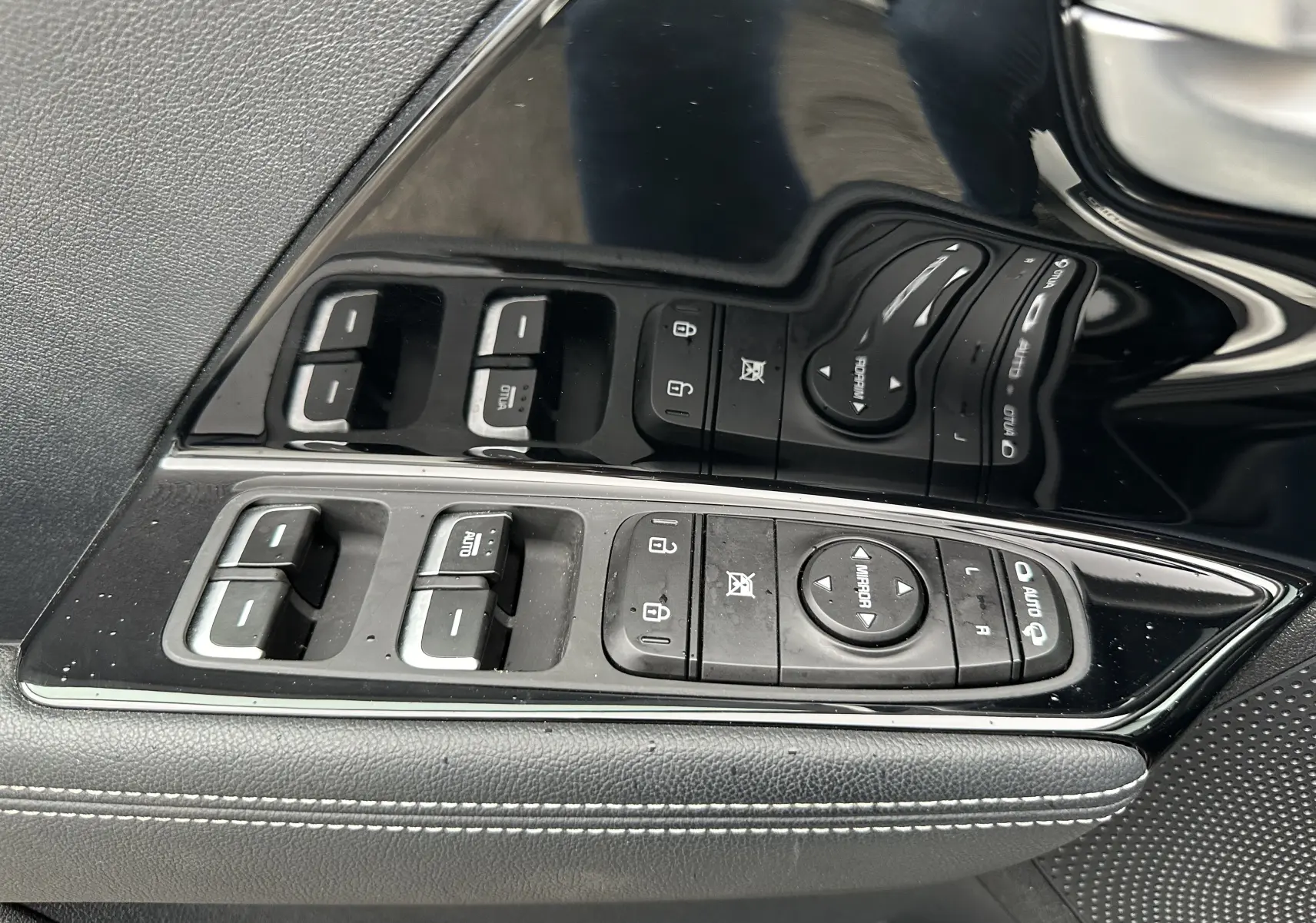 Gros plan sur les commandes de lève-vitres et réglage des rétroviseurs côté conducteur du Kia Niro blanc céleste 2020.