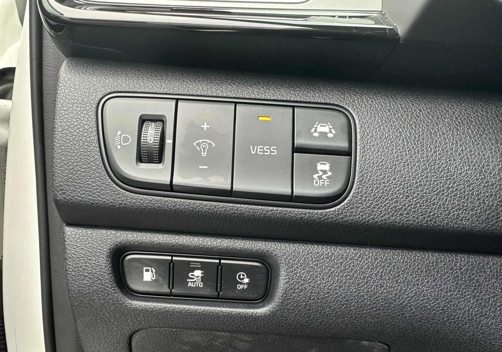 Gros plan sur les commandes noires du tableau de bord du Kia Niro hybride rechargeable blanc céleste, avec boutons d'assistance et réglages lumineux.