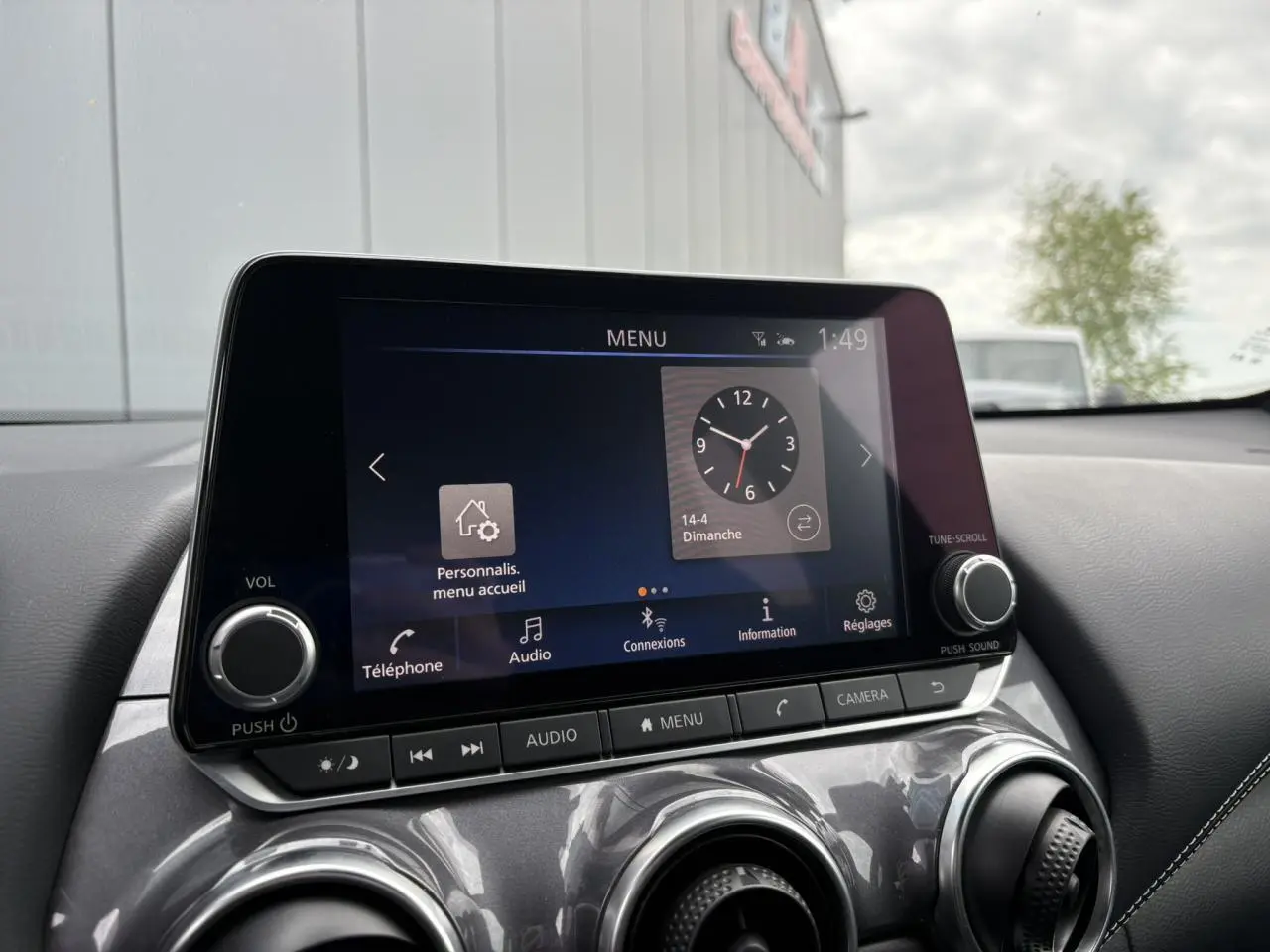 Écran tactile central du Nissan Juke 2023 affichant le menu principal avec commandes audio et caméra, intérieur noir.