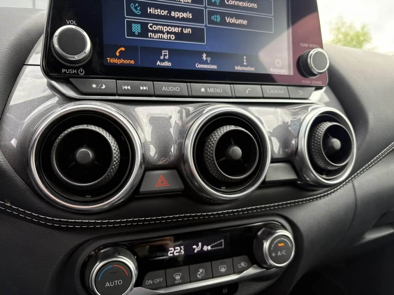 Gros plan sur la console centrale du Nissan Juke blanc perle 2023, affichant l'écran tactile et les commandes de climatisation.