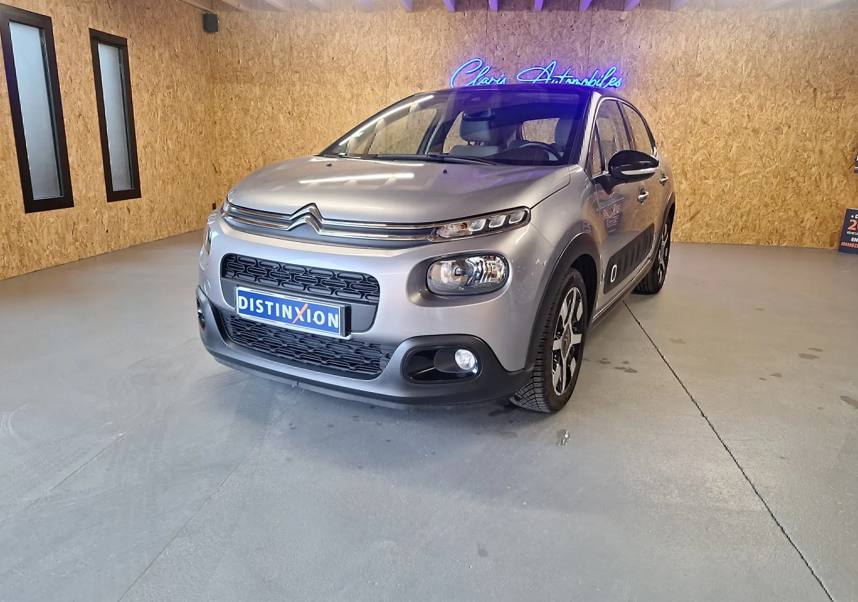 Citroën C3 gris en 3/4 avant droit dans un showroom avec jantes alu et rétroviseurs noirs brillants.