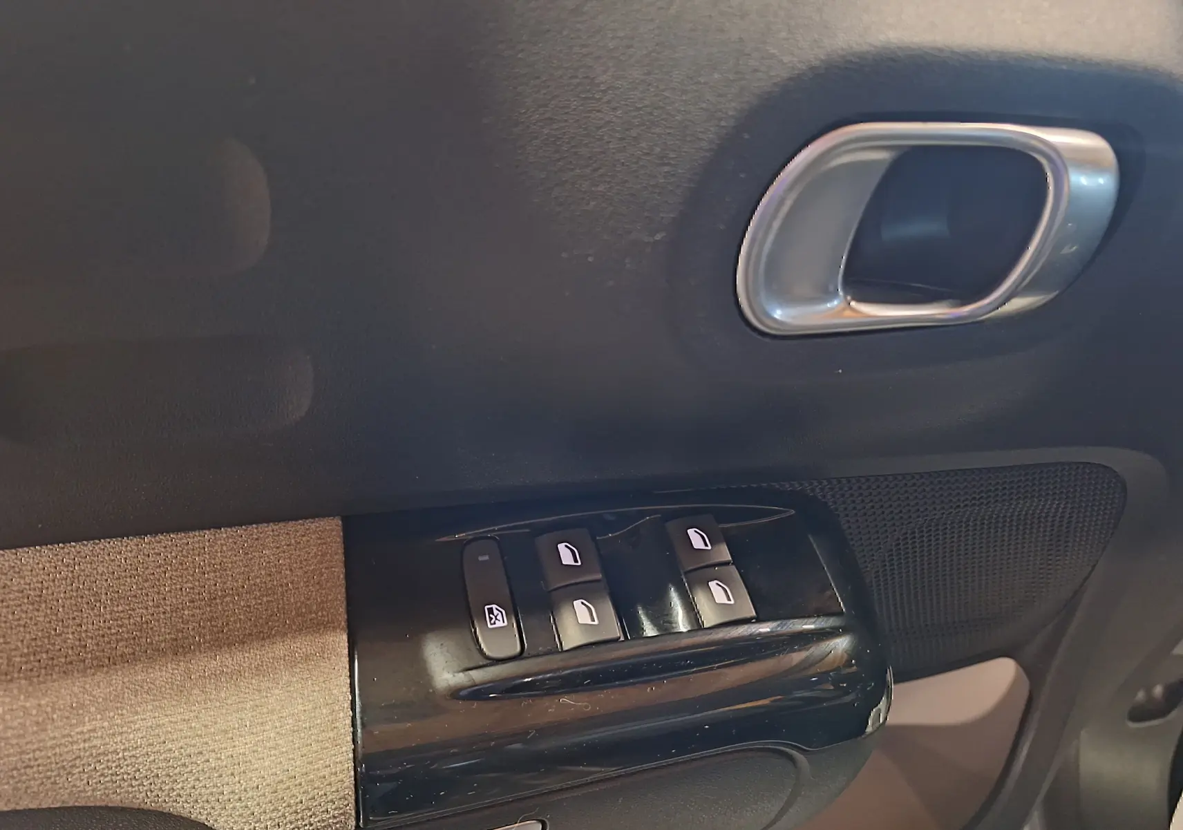 Gros plan sur la commande des vitres électriques et poignée intérieure côté conducteur du Citroën C3 gris 2019.