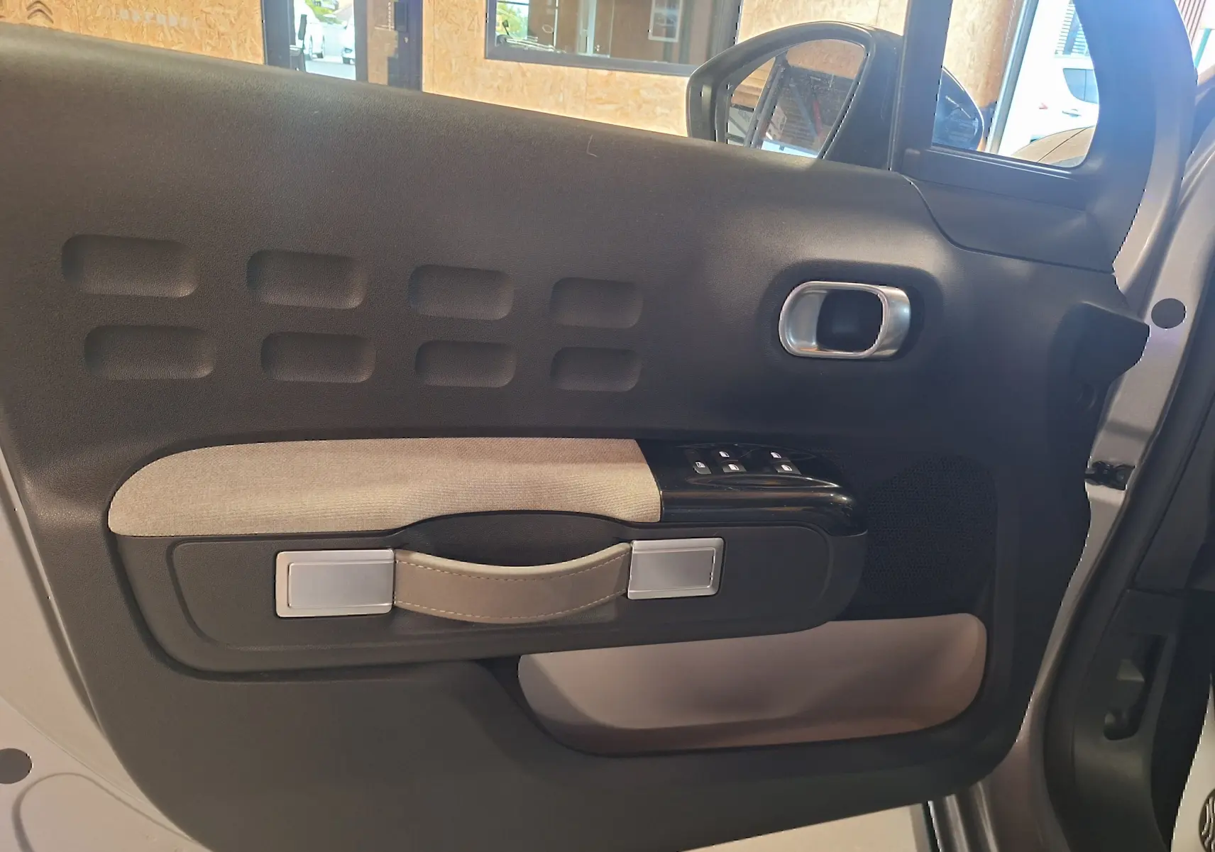 Gros plan sur la porte intérieure côté gauche d'une Citroën C3 gris, avec poignée en cuir et commandes de vitres.