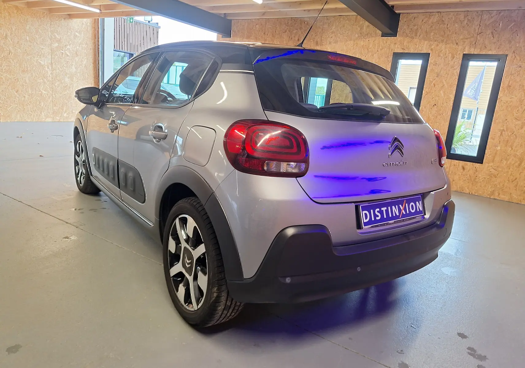 Vue 3/4 arrière droite d'une Citroën C3 gris avec toit noir et protections latérales noires en intérieur showroom.