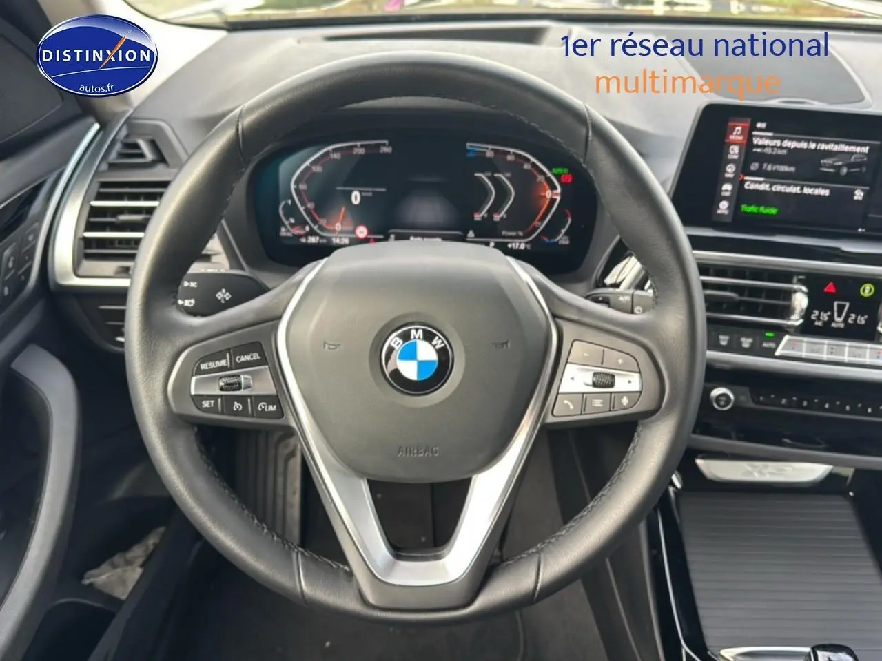 Vue centrée sur le volant cuir multifonction d'une BMW X3 2024, tableau de bord numérique et écran tactile visibles.