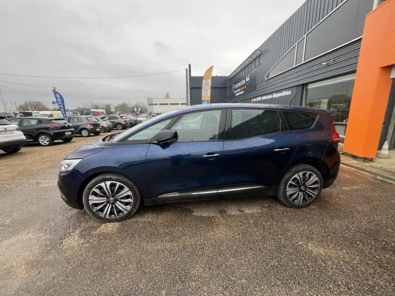 Profil côté gauche d'un Renault Grand Scenic bleu Cosmos 2022 garé devant un bâtiment commercial.