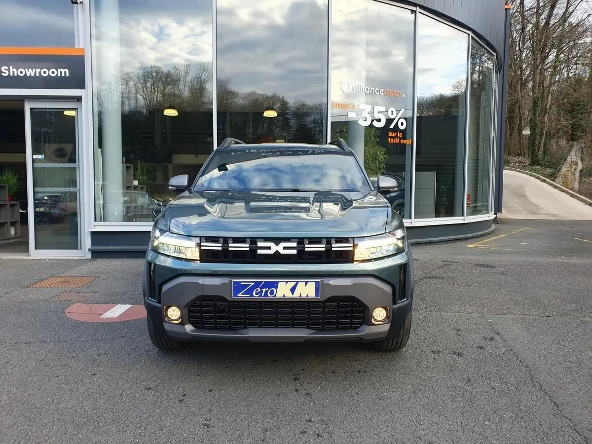 Vue frontale d'un Dacia Duster 2026 vert cèdre avec calandre noire et feux LED allumés devant un showroom.