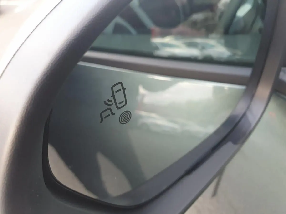 Rétroviseur extérieur gauche du Dacia Duster vert cèdre 2026 avec symbole d'alerte d'angle mort visible.