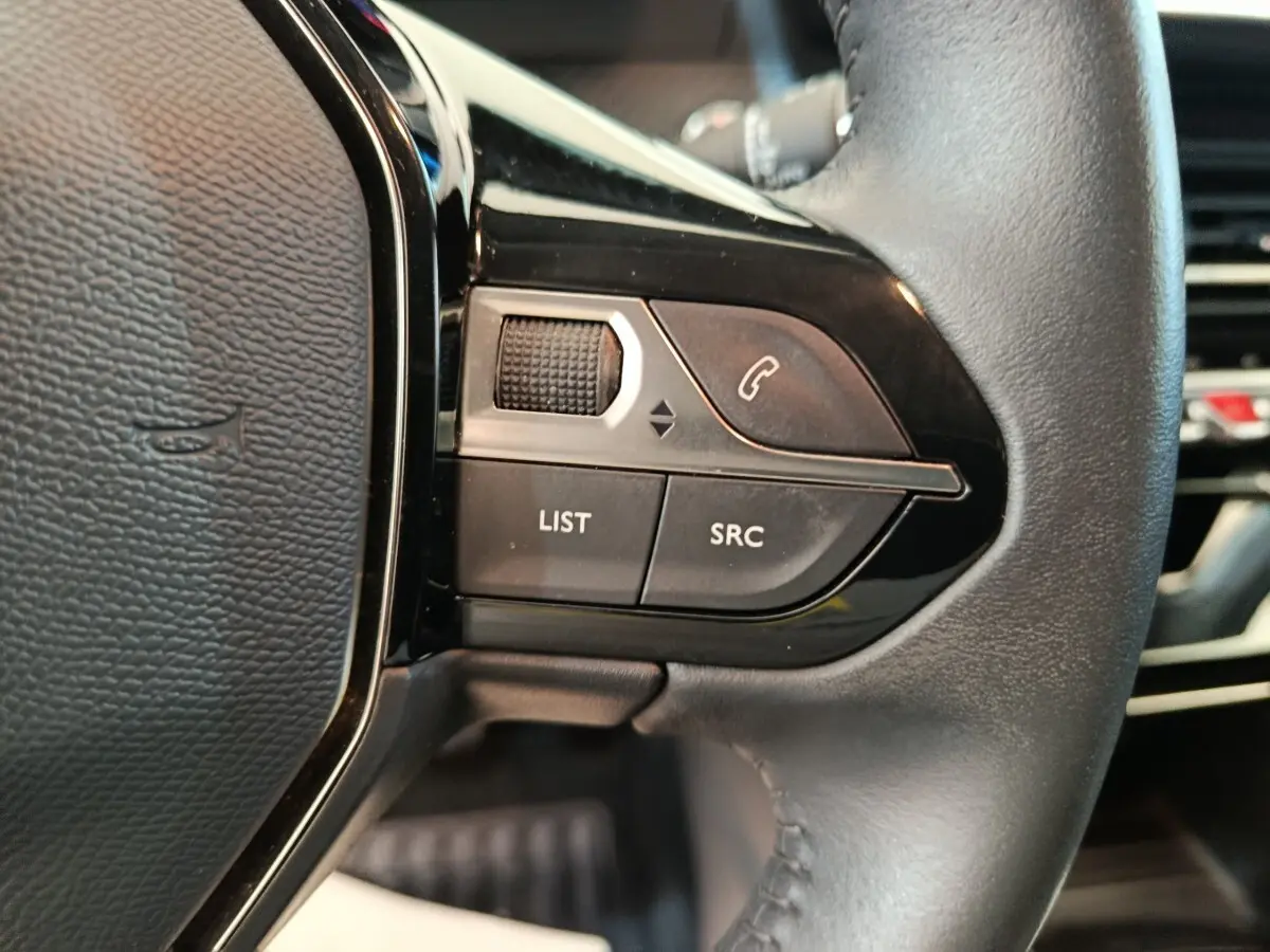 Gros plan sur les commandes gauche du volant cuir noir de la Peugeot 208 blanche PureTech 100 S&S Allure Business 2021.