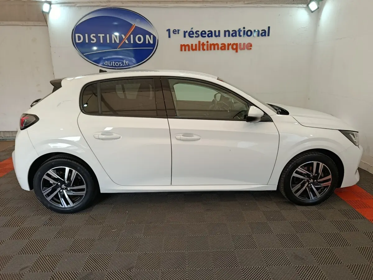 Vue latérale droite d'une Peugeot 208 blanche 2021 garée en intérieur, avec jantes alliage et vitres teintées.