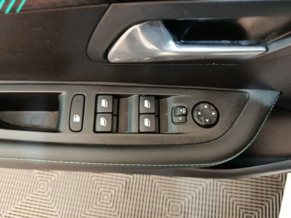 Vue rapprochée du panneau de commandes des vitres et rétroviseurs côté conducteur d'une Peugeot 208 blanche, intérieur noir.