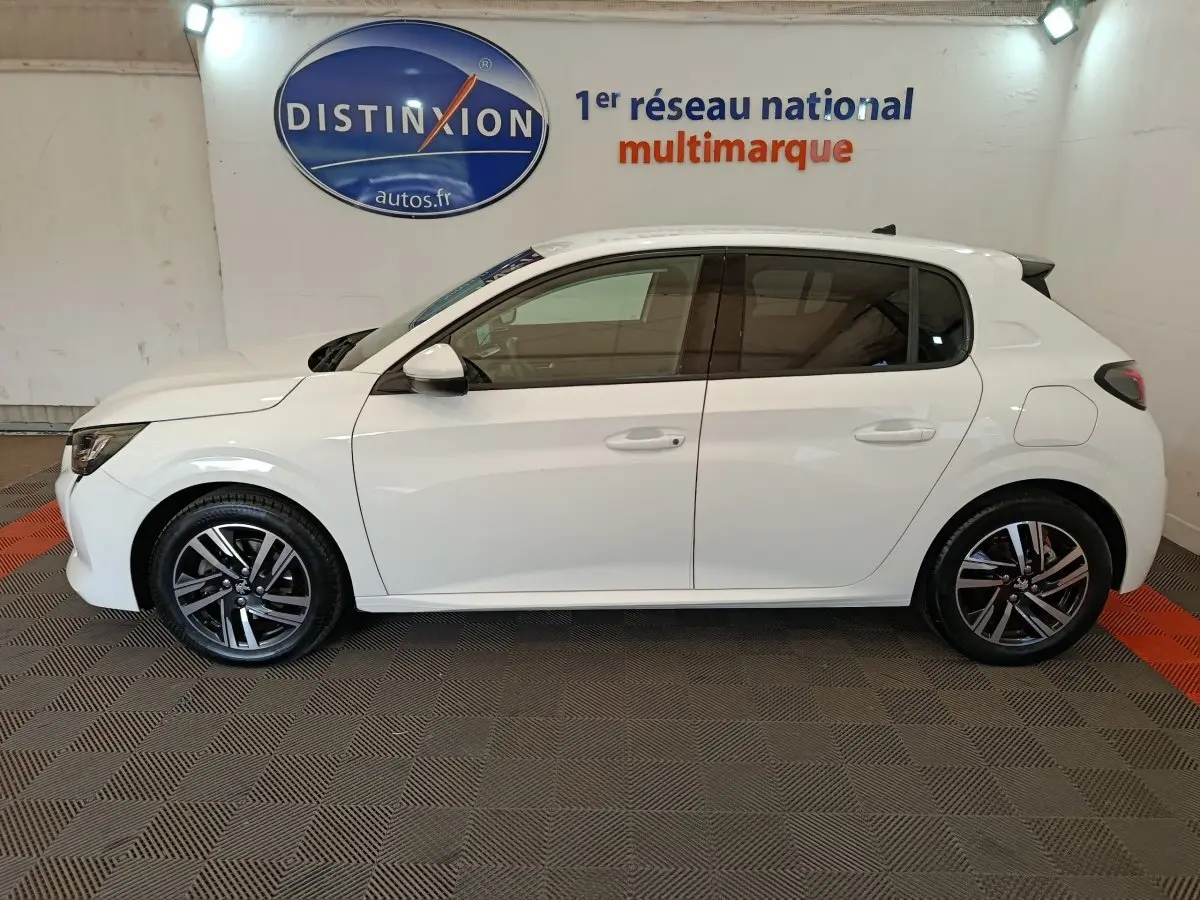 Peugeot 208 blanc vue de profil côté gauche, avec jantes alliage et vitres teintées, en intérieur showroom.