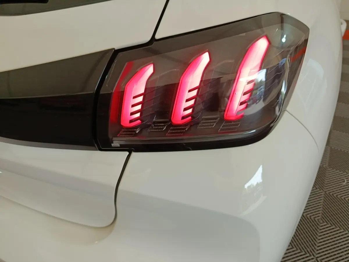Gros plan sur le feu arrière droit rouge allumé de la Peugeot 208 blanche, version PureTech 100 S&S Allure Business.