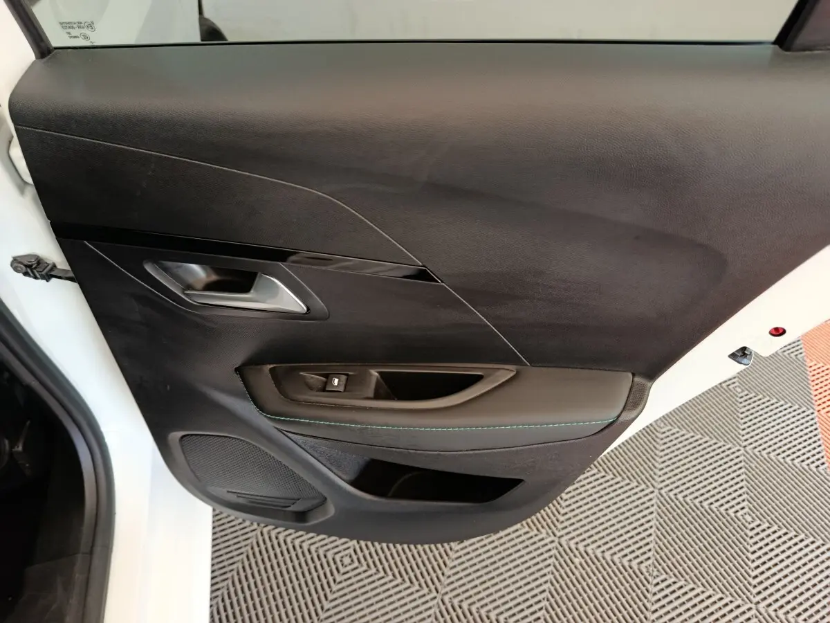 Vue rapprochée de la porte avant gauche noire avec poignée argentée et bouton de lève-vitre sur Peugeot 208 blanc.