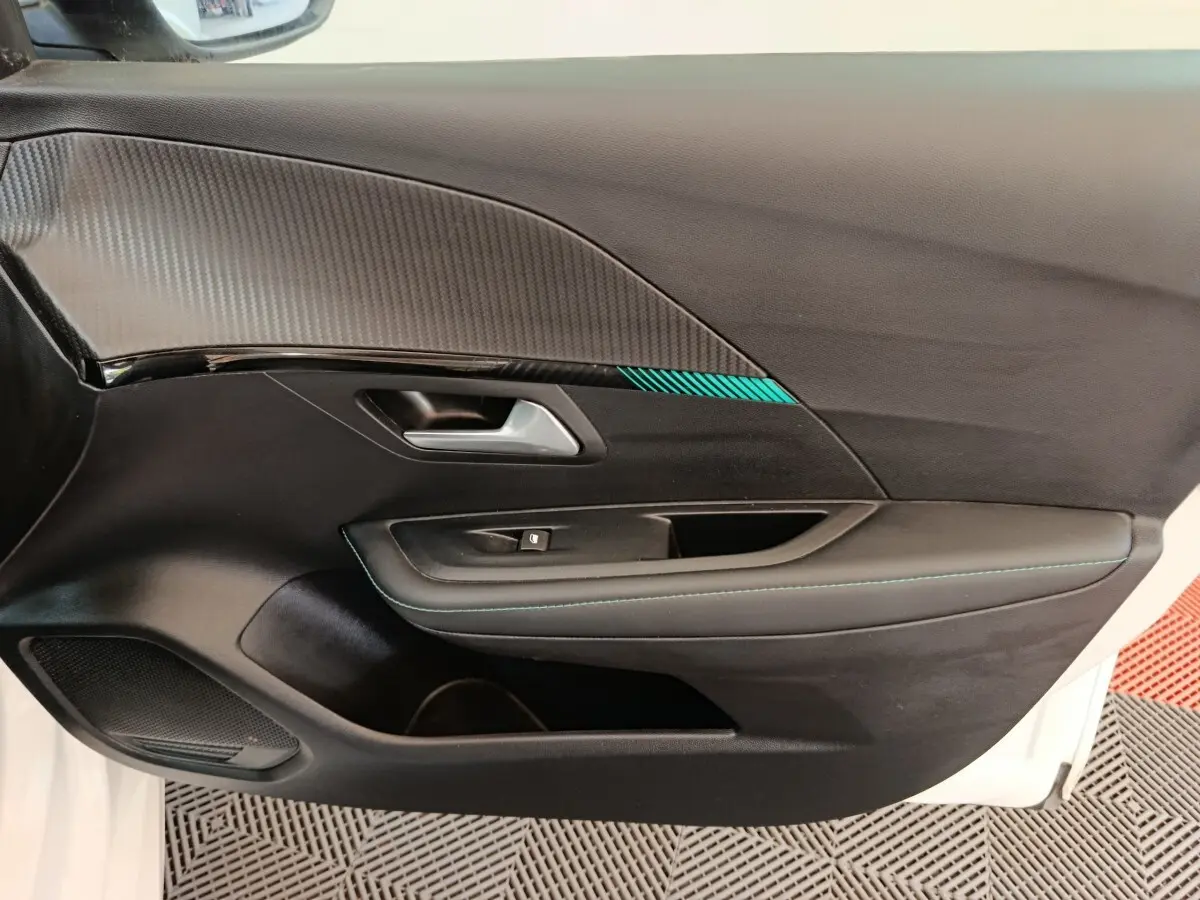 Vue rapprochée de la porte intérieure côté gauche d’une Peugeot 208 blanche avec surpiqûres bleues et insert décoratif.