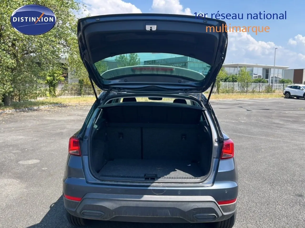 Vue arrière d'un SEAT Arona gris Magnetic Metal avec coffre ouvert sur un parking ensoleillé.