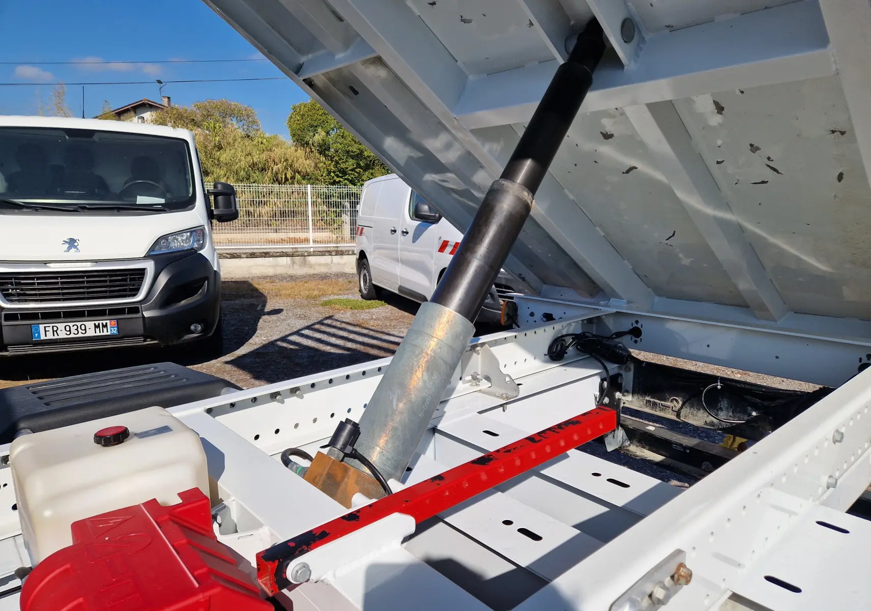 Gros plan sur la benne relevée blanche du Renault Master Châssis double cabine, montrant le vérin hydraulique et le coffre intégré.