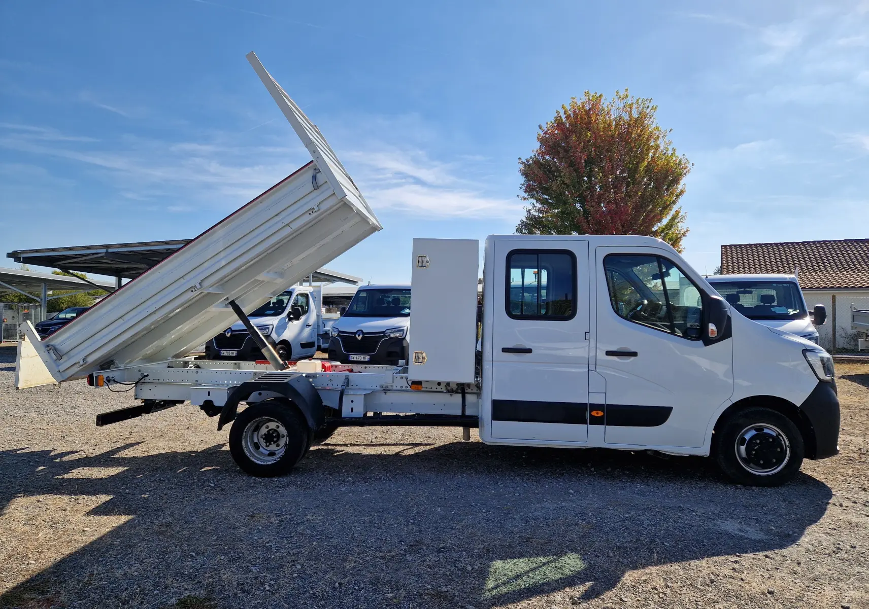 Vue latérale droite du Renault Master blanc avec benne relevée et coffre latéral, roues jumelées visibles.