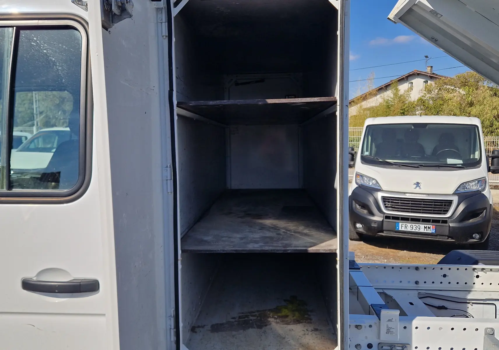 Vue rapprochée du coffre blanc ouvert d’un Renault Master Châssis double cabine avec benne relevée, côté gauche visible.