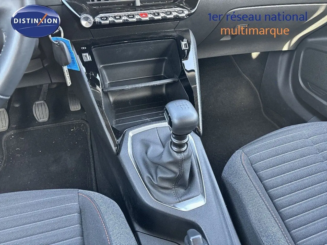 Gros plan sur la console centrale et levier de vitesse manuel d'une Peugeot 2008 gris Artense, sièges tissu noir à surpiqûres rouges.