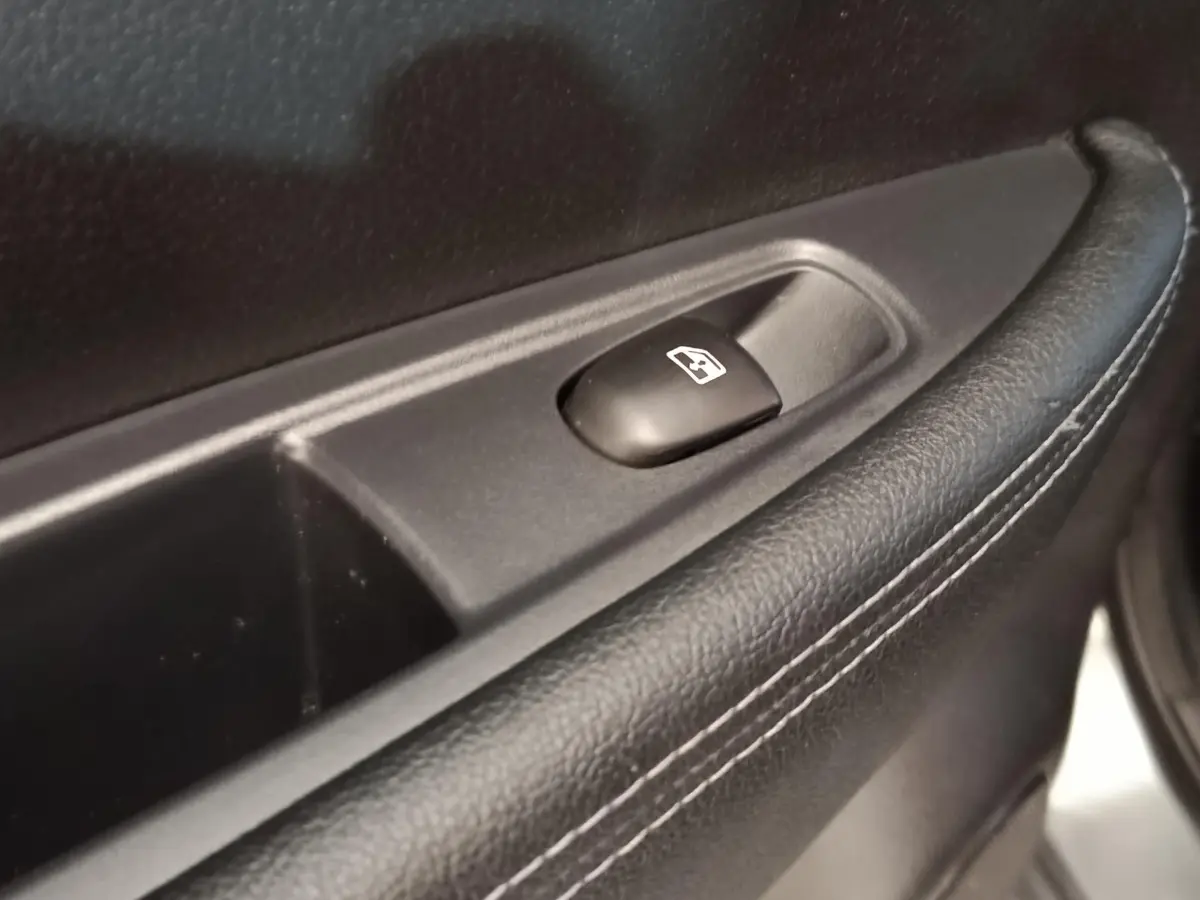 Détail du bouton de commande de la vitre électrique sur la porte intérieure en cuir noir du Nissan Qashqai gris clair.