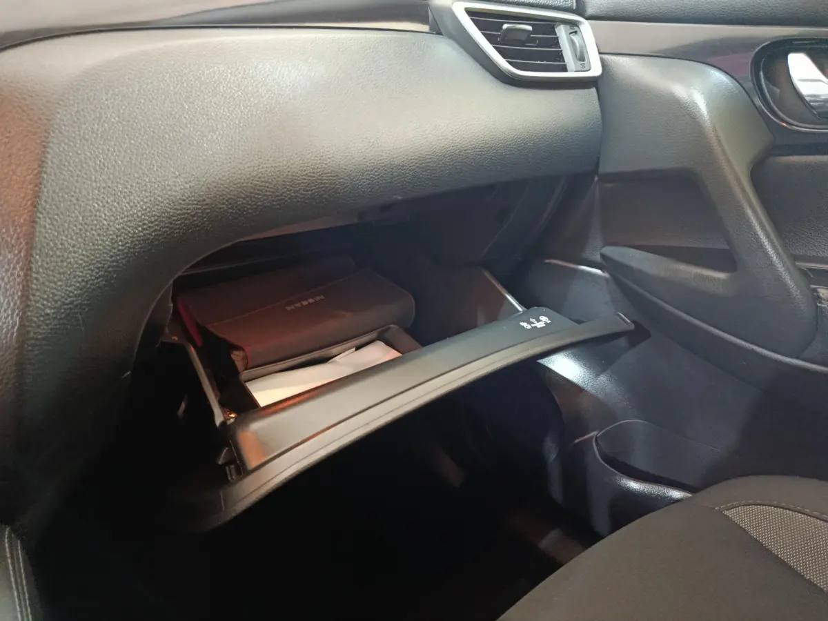 Intérieur du Nissan Qashqai 2019 gris clair, vue sur la boîte à gants ouverte côté passager avec manuel visible.