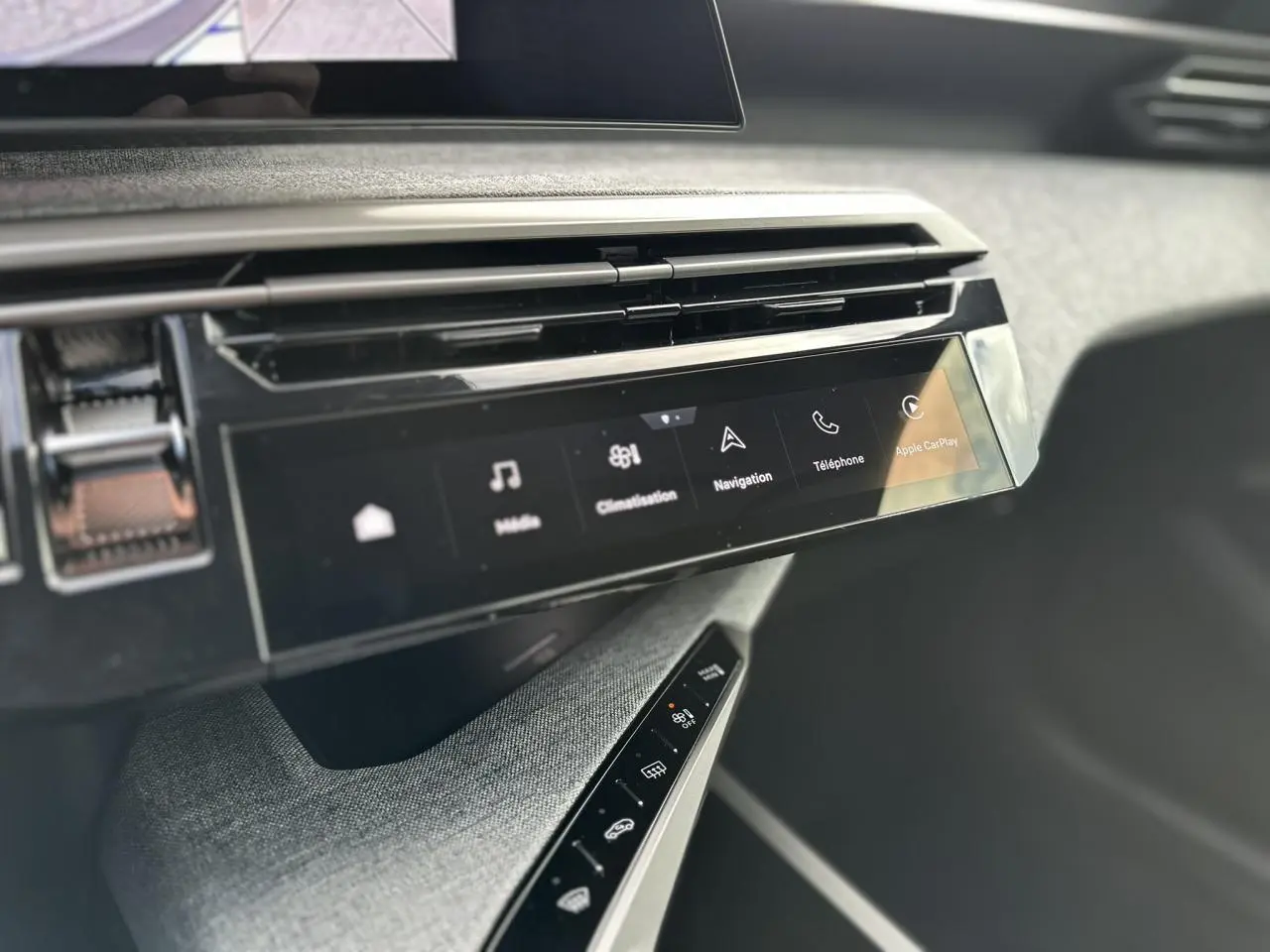 Vue rapprochée de la console centrale du Peugeot 3008 Hybrid 2025 avec écran tactile panoramique et commandes tactiles sur tissu gris.