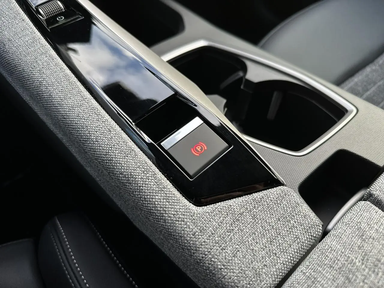 Gros plan sur la console centrale tissu gris chiné du Peugeot 3008 Hybrid 2025 avec bouton frein électrique rouge.