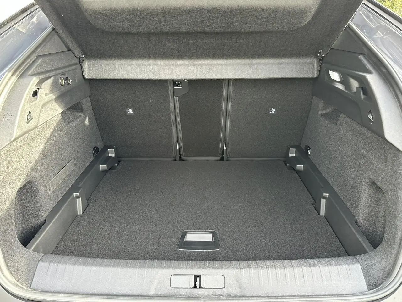 Coffre ouvert vu de l'arrière du Peugeot 3008 Hybrid gris Artense, espace de chargement vide et tapis noir.