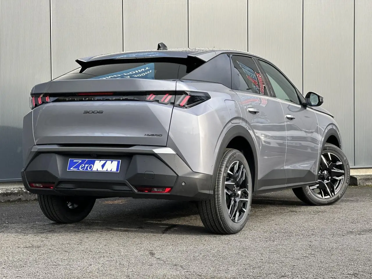 Vue 3/4 arrière droite d’un Peugeot 3008 Hybrid gris Artense avec feux arrière à LED en forme de griffes et jantes alliage noires.