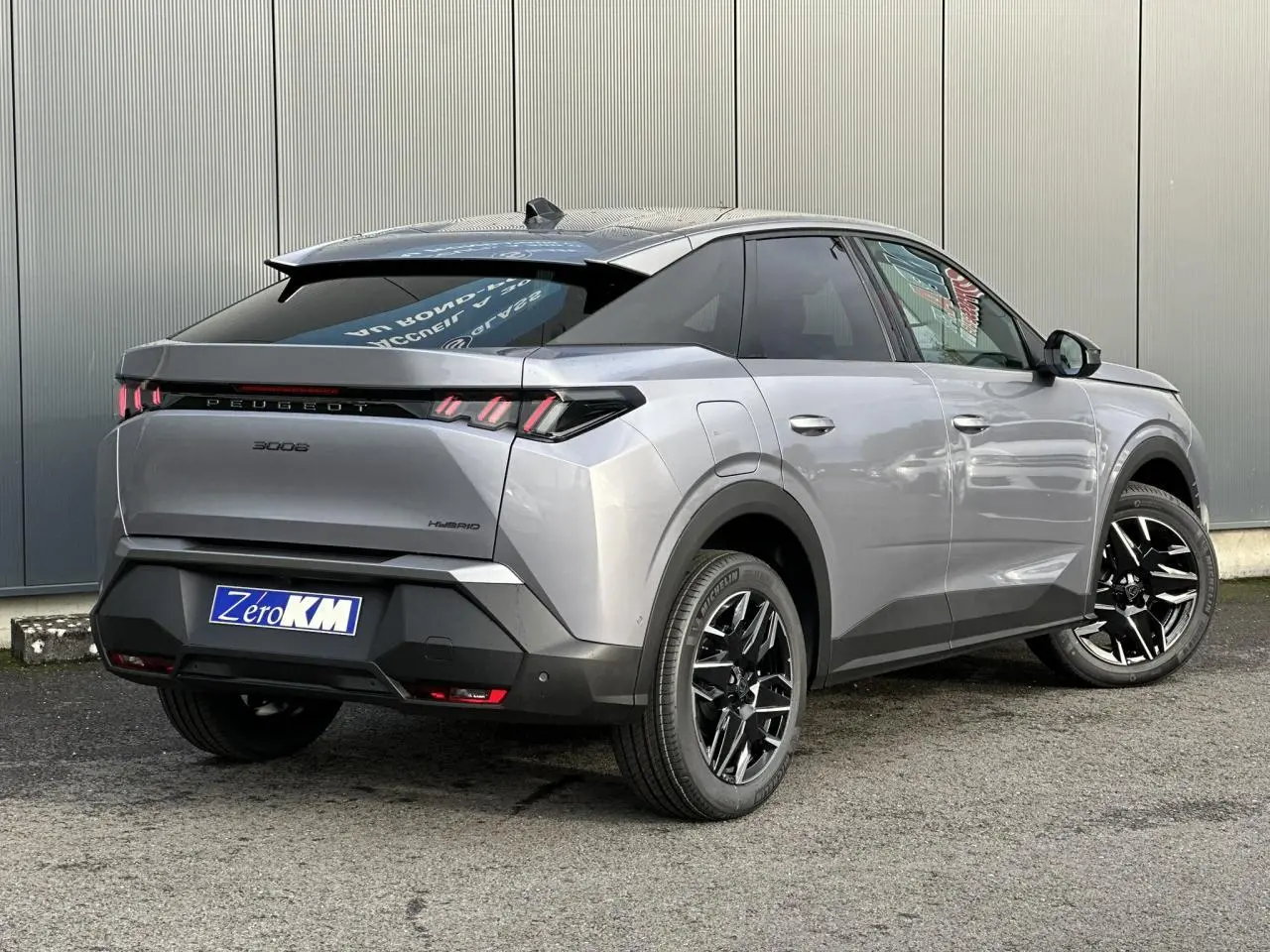 Vue 3/4 arrière droit d'un Peugeot 3008 Hybrid gris Artense avec jantes alliage noires et feux arrière LED 3 griffes.