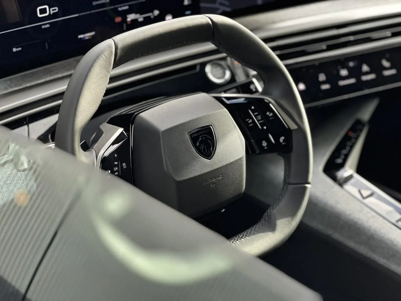 Gros plan sur le volant compact cuir noir avec logo Peugeot du Peugeot 3008 Hybrid 2025, intérieur moderne et écran panoramique visible.