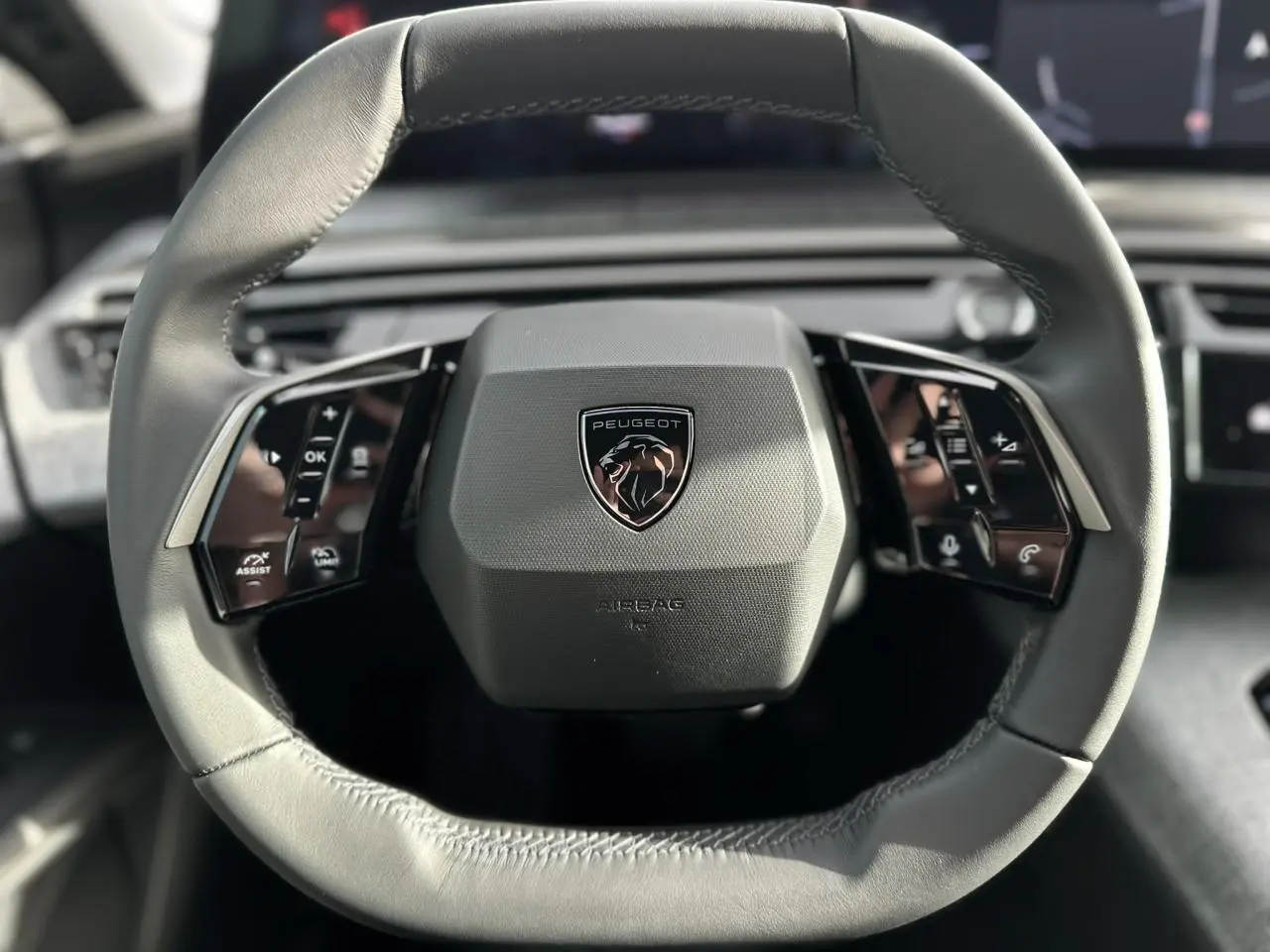 Gros plan sur le volant cuir gris du Peugeot 3008 Hybrid 2025 avec commandes intégrées et logo lion central.