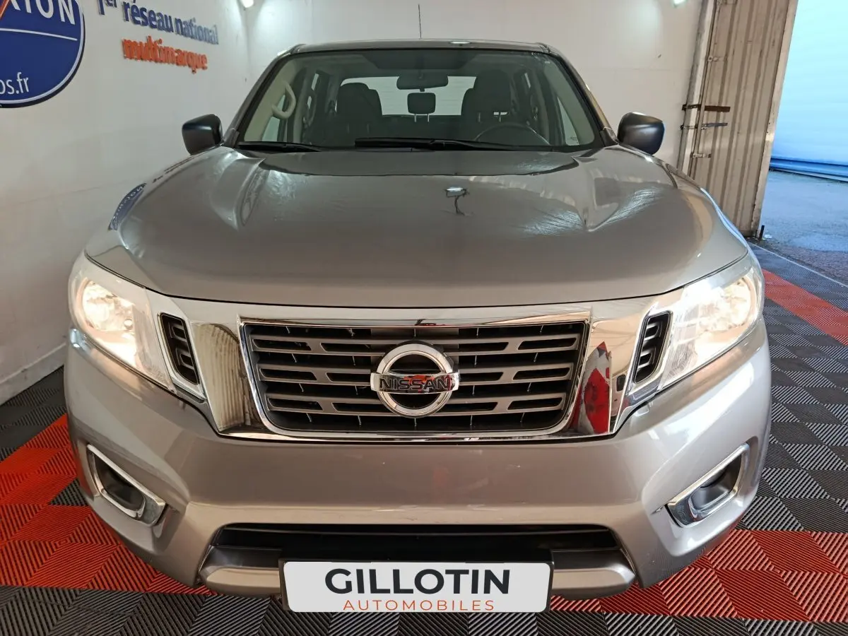 Vue avant d'un Nissan Navara Double-Cab gris clair, mettant en valeur sa calandre chromée et ses phares allumés.