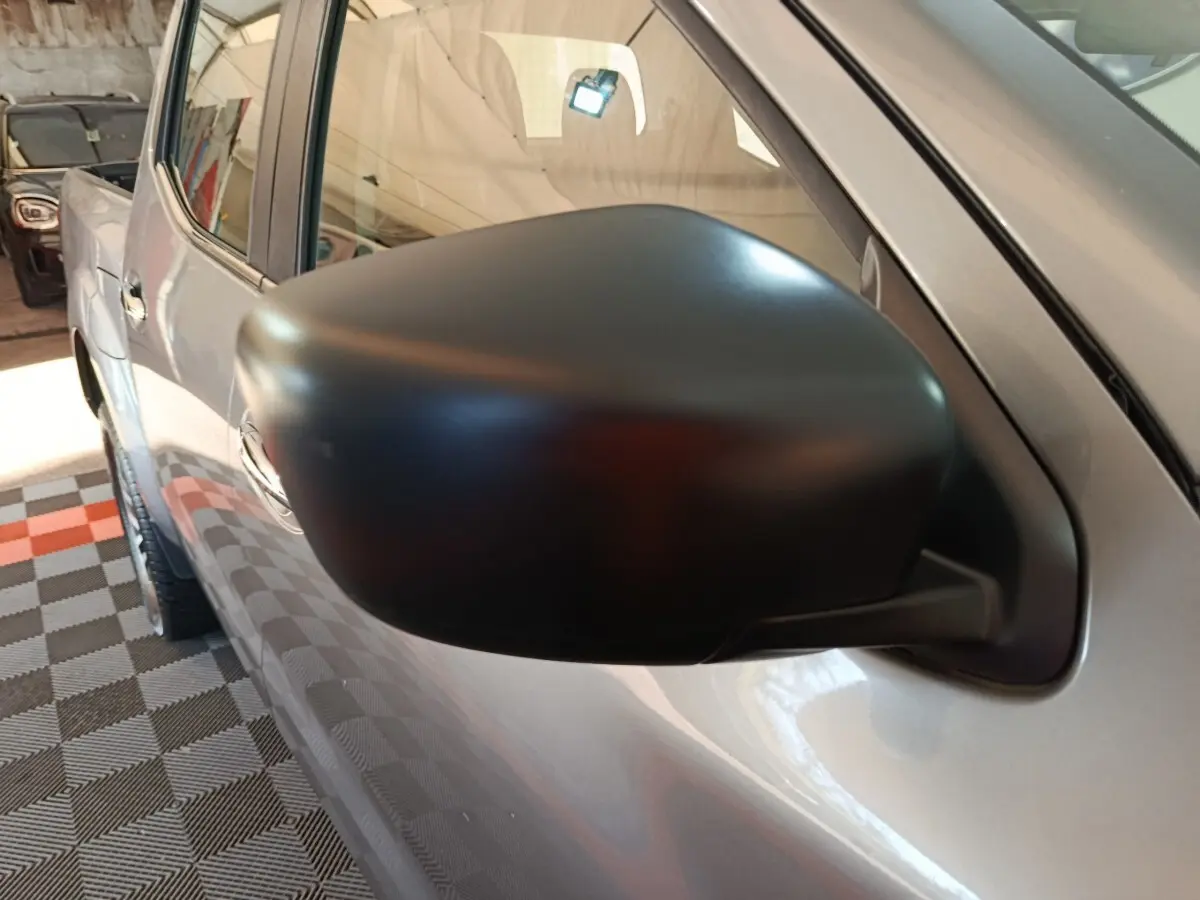Gros plan sur le rétroviseur côté gauche noir mat du Nissan Navara gris clair, vue partielle de la porte avant.