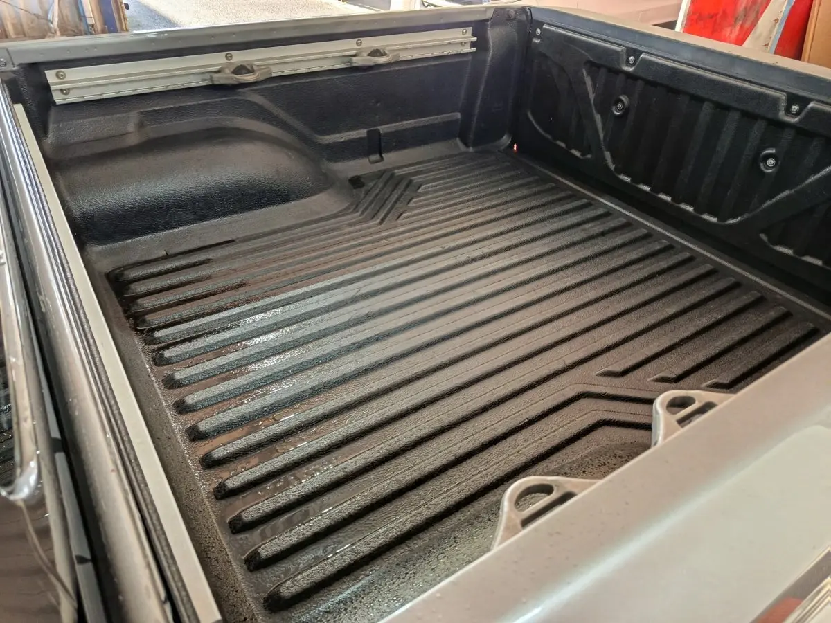 Vue rapprochée de la benne noire du Nissan Navara gris clair, montrant les ridules et crochets de retenue.