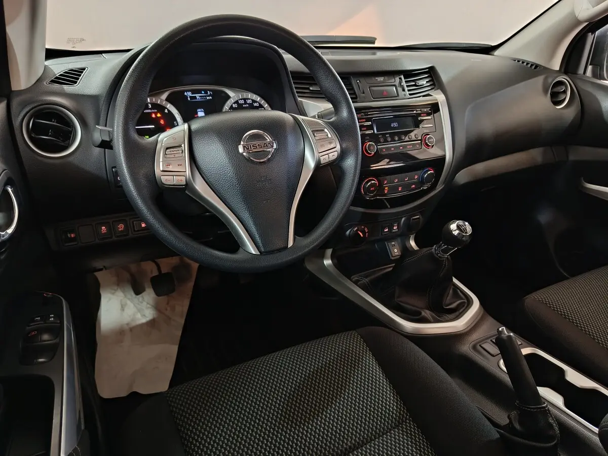 Vue intérieure centrée sur le volant multifonctions et la console centrale d’un Nissan Navara 2018, sièges noirs.
