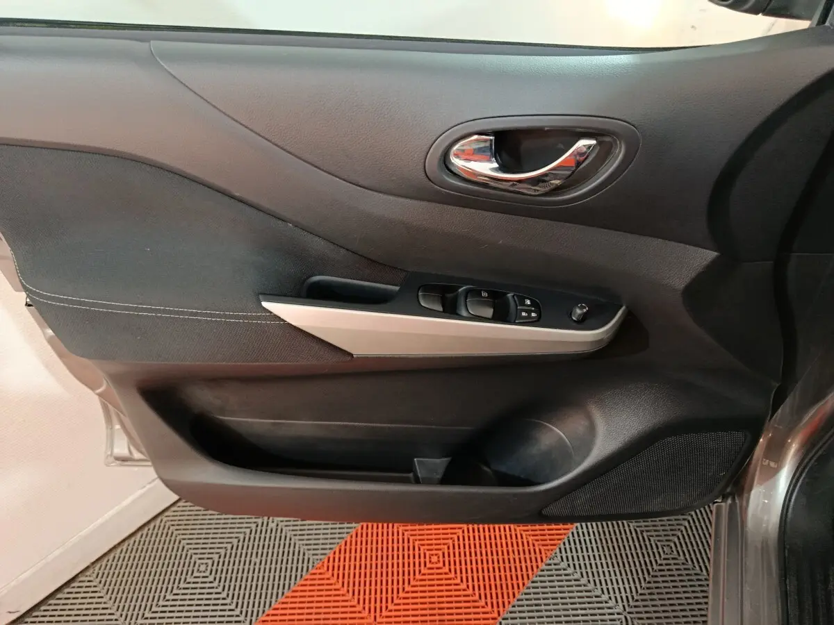 Vue intérieure côté gauche de la porte avant d'un Nissan Navara gris clair avec commandes de vitres et poignée chromée.