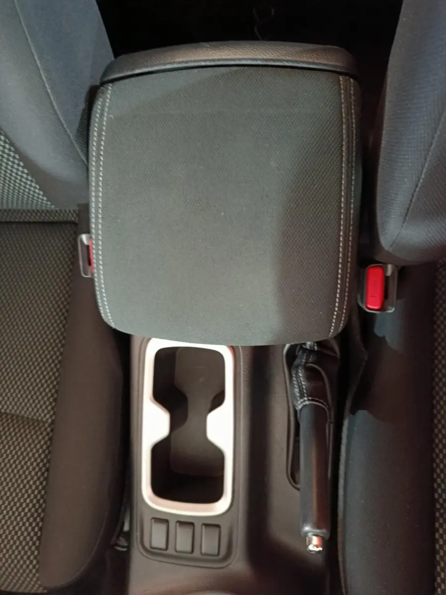 Vue plongeante sur la console centrale noire du Nissan Navara avec accoudoir, frein à main et porte-gobelets.